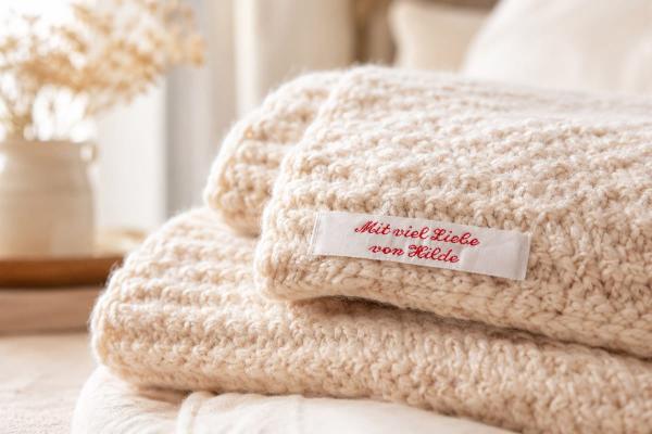 Weißes Baumwoll-Etikett mit roter Schrift auf Strickdecke